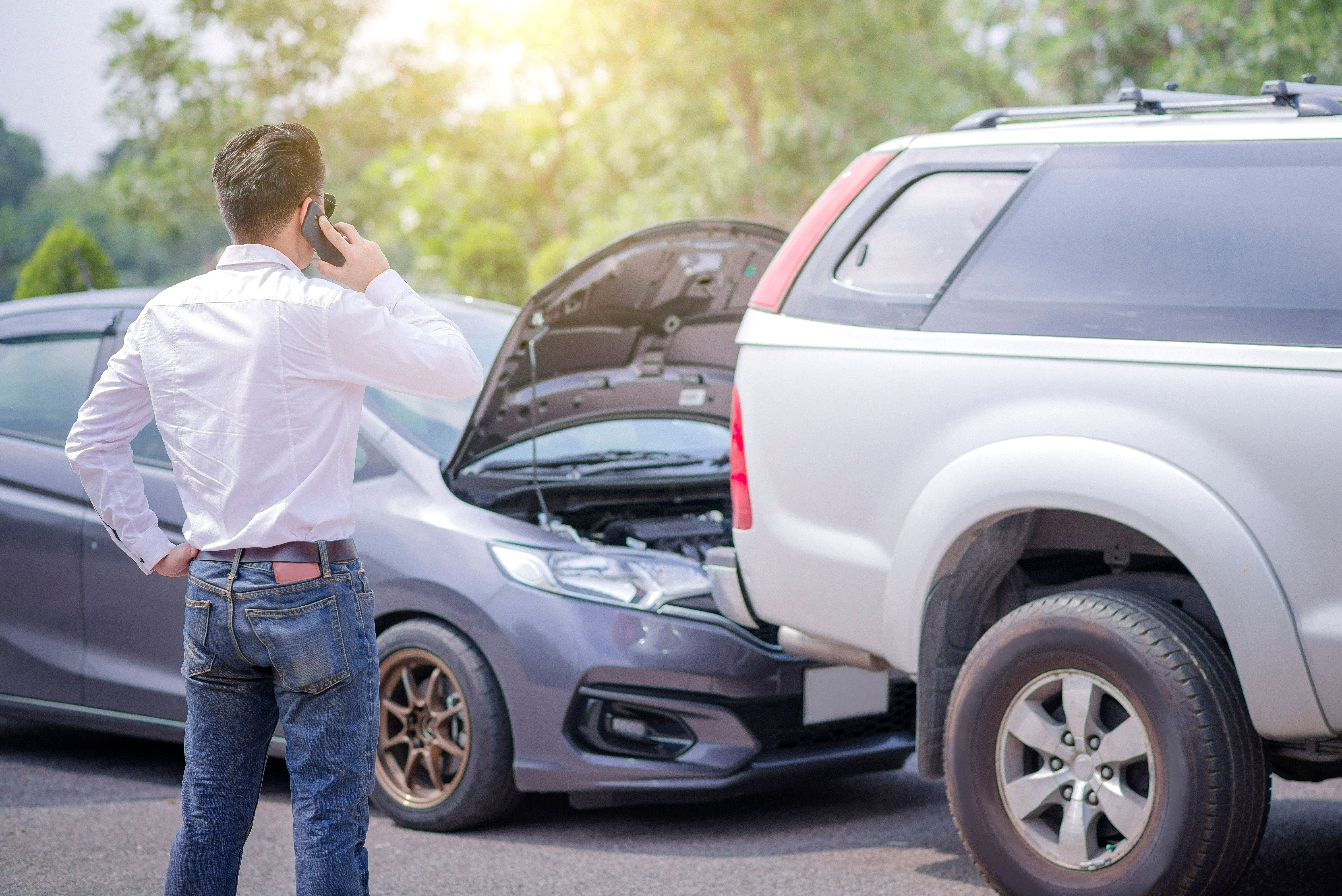 An image of a man standing in front of an accident on a phone calling a rideshare accident law firm.